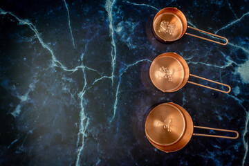 Three of copper measuring cups on dark blue marble background in top view