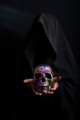 Human skull shining with varnish on the palms of an unknown person under a hood, a mystical,...