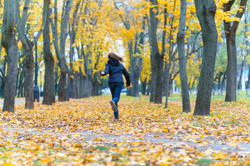 a girl running through the park and enjoys autumn, beautiful nature with yellow leaves