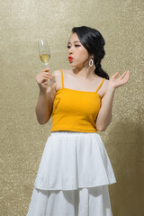 Young happy woman looking away and smiling with champagne isolated over gold background.