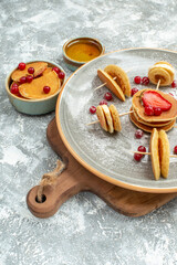 Side view of delicious pancakes with fruits on wooden cutting board and honey on blue background