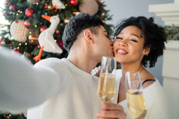 a man and a woman are photographed against the background of a Christmas tree. They hold champagne glasses in their hand, smile and are in a good mood. Celebrate the new year together 