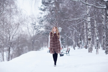 Fototapeta premium girl in a fur vest walks in the winter outside / adult young model in winter clothes fur