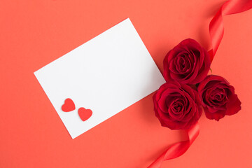 Top view of empty white paper for text, red roses and hearts on the red background