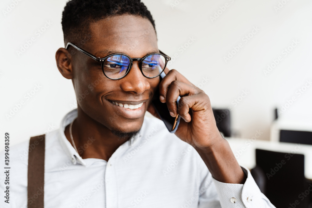 Poster Afro american pleased man in eyeglasses talking on mobile phone