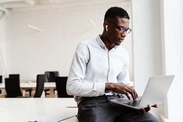 Afro american serious man in earphones working with laptop