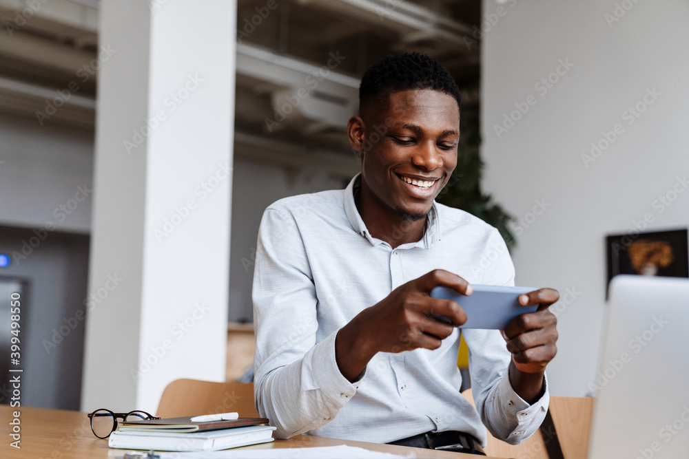 Poster Afro american joyful man smiling and using mobile phone