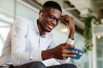 Afro american man in eyeglasses holding cellphone while sitting indoor