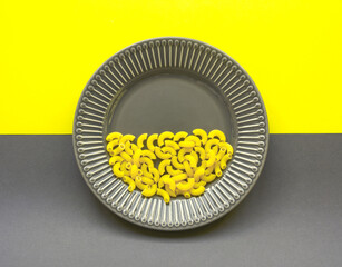 Illuminating und ultimate gray. Color of year 2021. Gray plate with yellow Italian pasta (macaroni) on yellow and gray background. Creative trendy food concept. Minimalism aesthetic