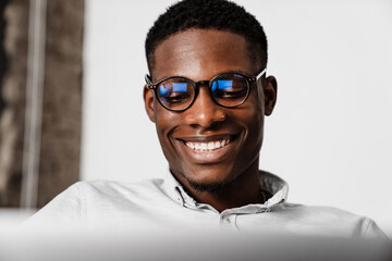 Afro american man in eyeglasses smiling and working with laptop indoors