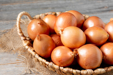 Onions in the basket. Onions in a wicker basket on a wooden table. Onion plant closeup	