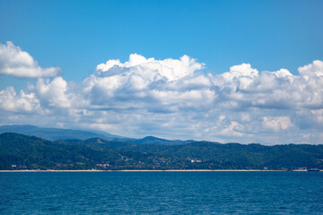 Sea and mountains against the blue sky with white clouds, at the bottom of the mountains are buildings