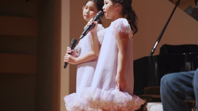 confident asian sister singing duo song in the show. happy girls band music performance. lovely daughter in same dress sing a song together.