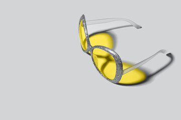 Trending colors of 2021. Plastic sunglasses with silver sparkles frame and yellow glasses. Yellow color shadow from glasses