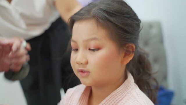 happy asian girl having face makeup by artist. confident kid feels satisfy when beautiful. 