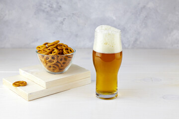 A glass of light beer with pretzels on a light wooden background - obrazy, fototapety, plakaty