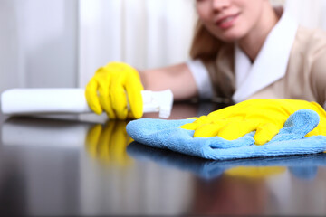 Cleaning in the hotel or in the house. Maid in protective gloves wipes furniture in the room. White plastic bottle in hand. Out of focus. Unrecognizable person.