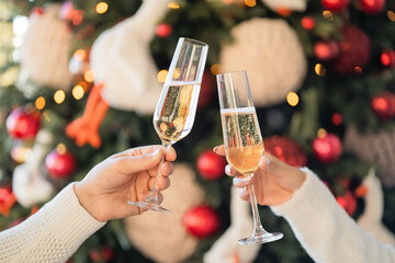 a toast to the holiday. a couple of friends hold glasses with a champagne drink and clink glasses. celebrate holidays. Christmas tree with toys is decorated for Christmas. space for banner