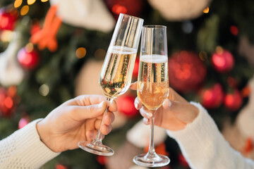 a toast to the holiday. a couple of friends hold glasses with a champagne drink and clink glasses. celebrate holidays. Christmas tree with toys is decorated for Christmas. copy space