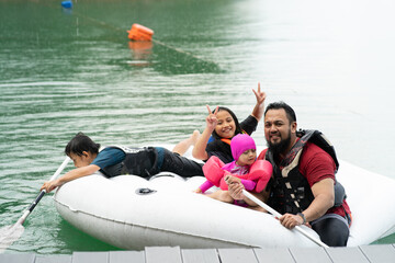 Naklejka premium Family wearing life jackets paddling on an inflatable boat in Kenyir Lake, Malaysia.