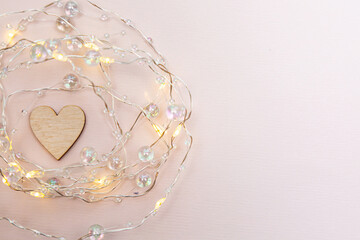 Wooden heart with lights garland on a gentle pink background. Happy valentine's day card. Valentine's Day.