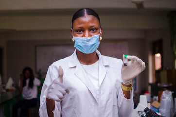 young beautiful african doctor wearing face mask holding vaccine, cure of the outbreak in the...