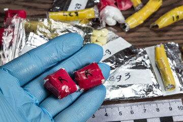 evidence of smuggling traffic: Packaging of a narcotic substance in the hand of a forensic expert against the background of other arrested materials, cocaine, heroin, spice