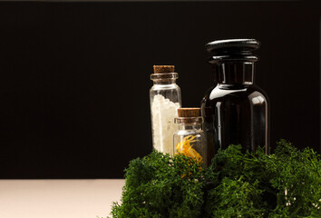 Bottles of spa salt, beauty ingredients, green plant against dark background.Empy space
