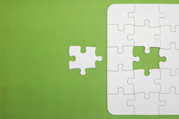 incomplete white puzzle with green background. missing a piece to complete that is next to it. has space for text. copy for space