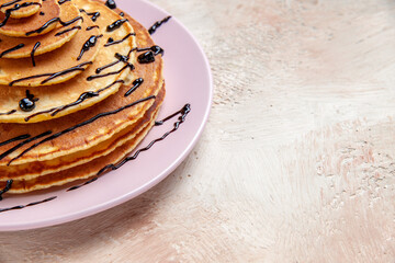 Half shot of stuffy pancakes decorated with chocolate syrup on a white background