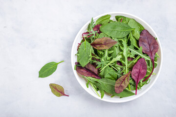 Healthy salad, leaves mix salad of spinach, arugula, lettuce in white plate on grey table .