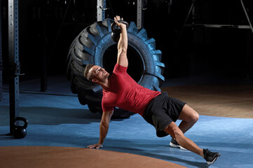 Attractive sportsman with kettle bell exercise in the fitness gym on the dark background. Copyspace...