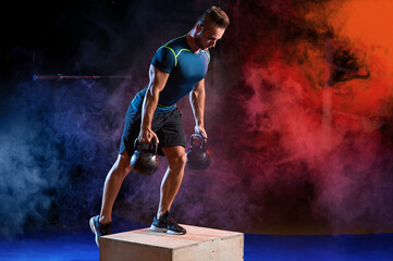 Attractive sportsman with kettle bell exercise in the fitness gym on the color smoke background. Copyspace area for advertise slogan or text message. Functional training and crossfit concept.