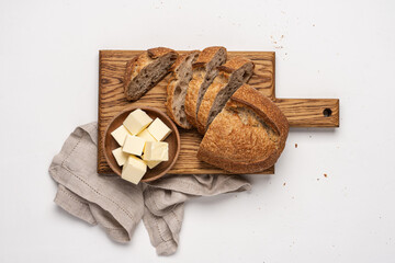 Sliced bread on cutting board and pieces of butter in wooden bowl on white background. Simple food breakfast