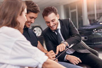 Laughing couple signing contract with auto dealer