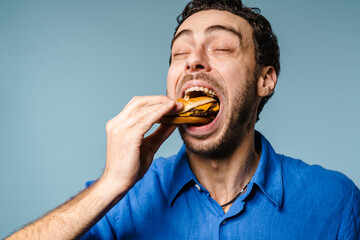 Excited handsome hungry guy eating hamburger on camera