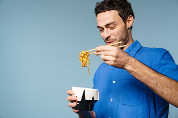 Joyful handsome guy smiling while eating asian noodles takeaway