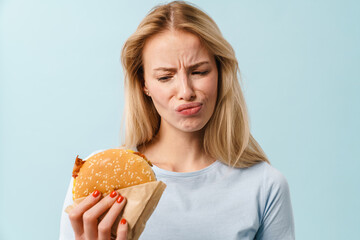 Displeased beautiful blonde girl posing with hamburger - obrazy, fototapety, plakaty