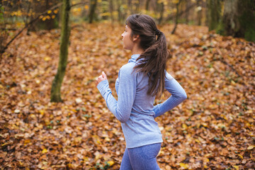 young sporty female running in beautiful autumn forest. Exercising outdoors in cold weather