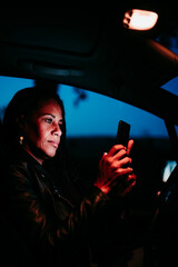 hispanic woman using mobile phone in car at night. Travel and technology concept