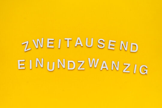 Zweitausendeinundzwanzig in Holzbuchstaben in Deutsch geschrieben auf einem gelben Hintergrund. Neues Jahr, Draufsicht.