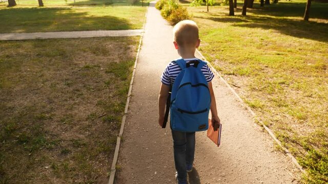 schoolboy boy goes through the park with a backpack and a textbook to school. kid dream education study concept. school boy going to school. schoolboy kid going home through the park dream fun