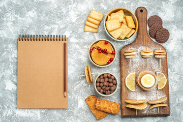 Obraz na płótnie Canvas Simple pancakes with lemons on cutting board and cookies and notebook on blue background