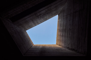 Massive concrete building overlooking the blue sky. Abstract contemporary geometric architecture. Bring in the light to the dungeon. Concept photo. Horizontal photo.