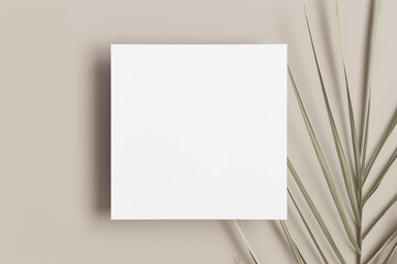 Square invitation card mockup with a palm leaf on a beige table.