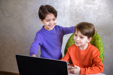 Happy overjoyed boy with his friend screaming excitedly, keeping fists pumped while playing video games on laptop pc, cheering after he won, his little brother smiling joyfully in background.