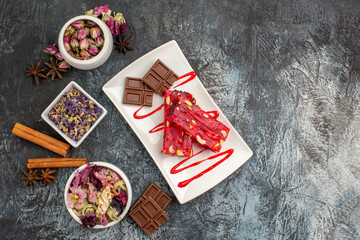 a plate of chocolate and bowls of dried flowers around it on grey background