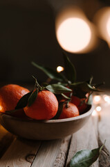 Sweet ripe tangerines on wooden table with christmas lights on dark background