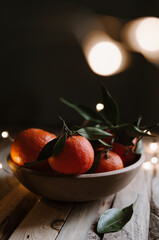 Sweet ripe tangerines on wooden table with christmas lights on dark background