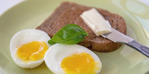 Two soft-boiled egg halves on a plate. Basil leaf, toast and butter. Close up.